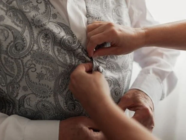 Hands helping a senior button his vest